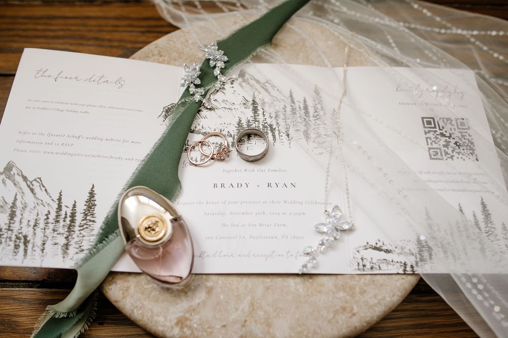 Wedding invitation suite with greenery and rings photographed on wooden surface.
