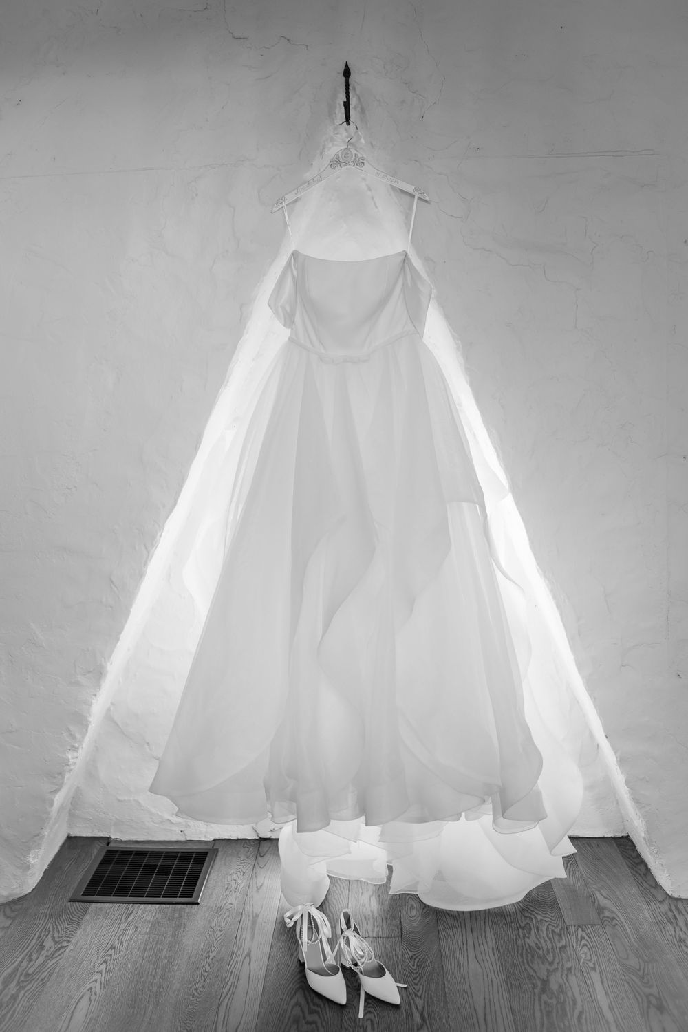 White wedding dress and shoes displayed elegantly against a light wall and wooden floor.