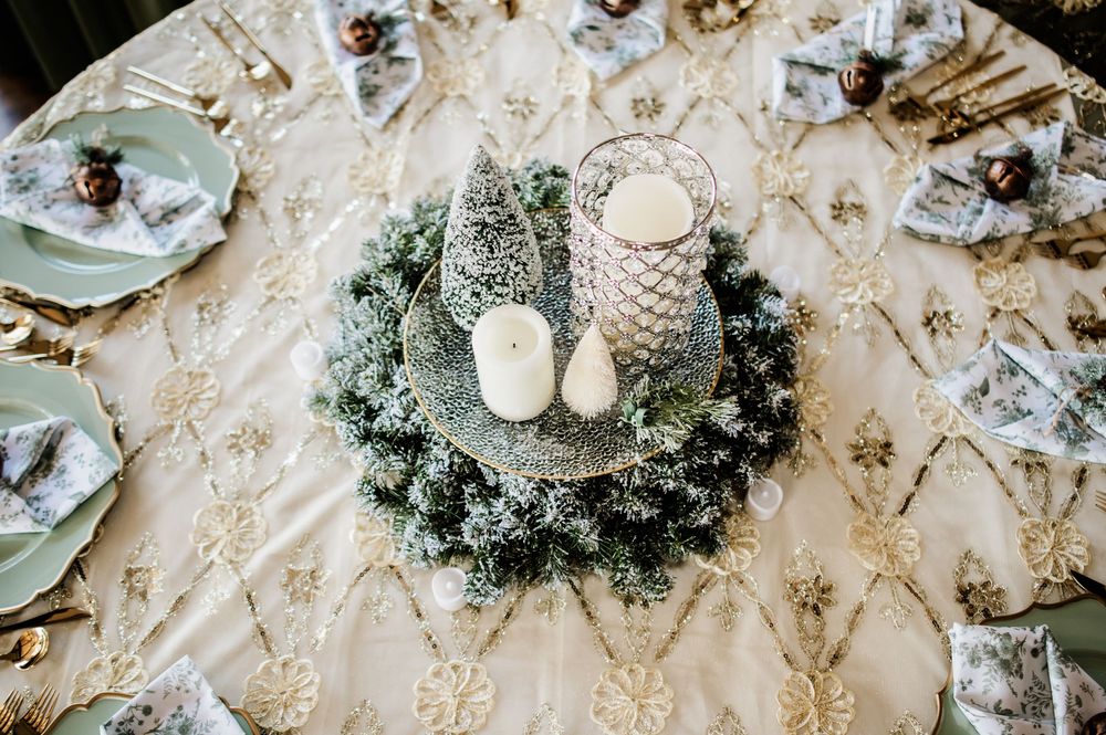 White and silver table settings with ornate patterns and winter greenery centerpieces.