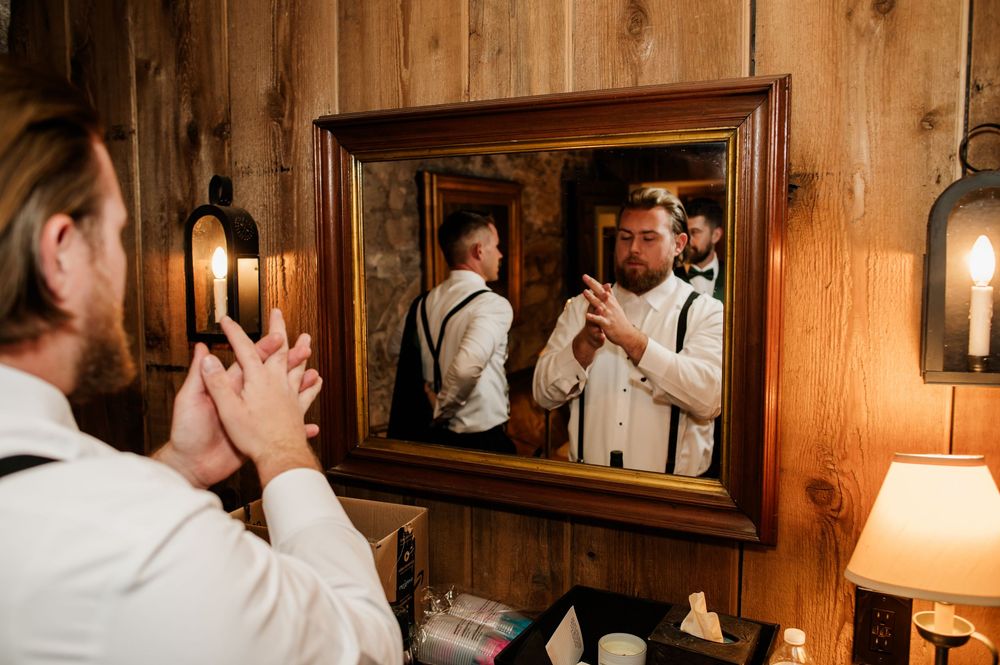 Wedding party members adjusting their formal attire in front of a mirror in a wooden room.