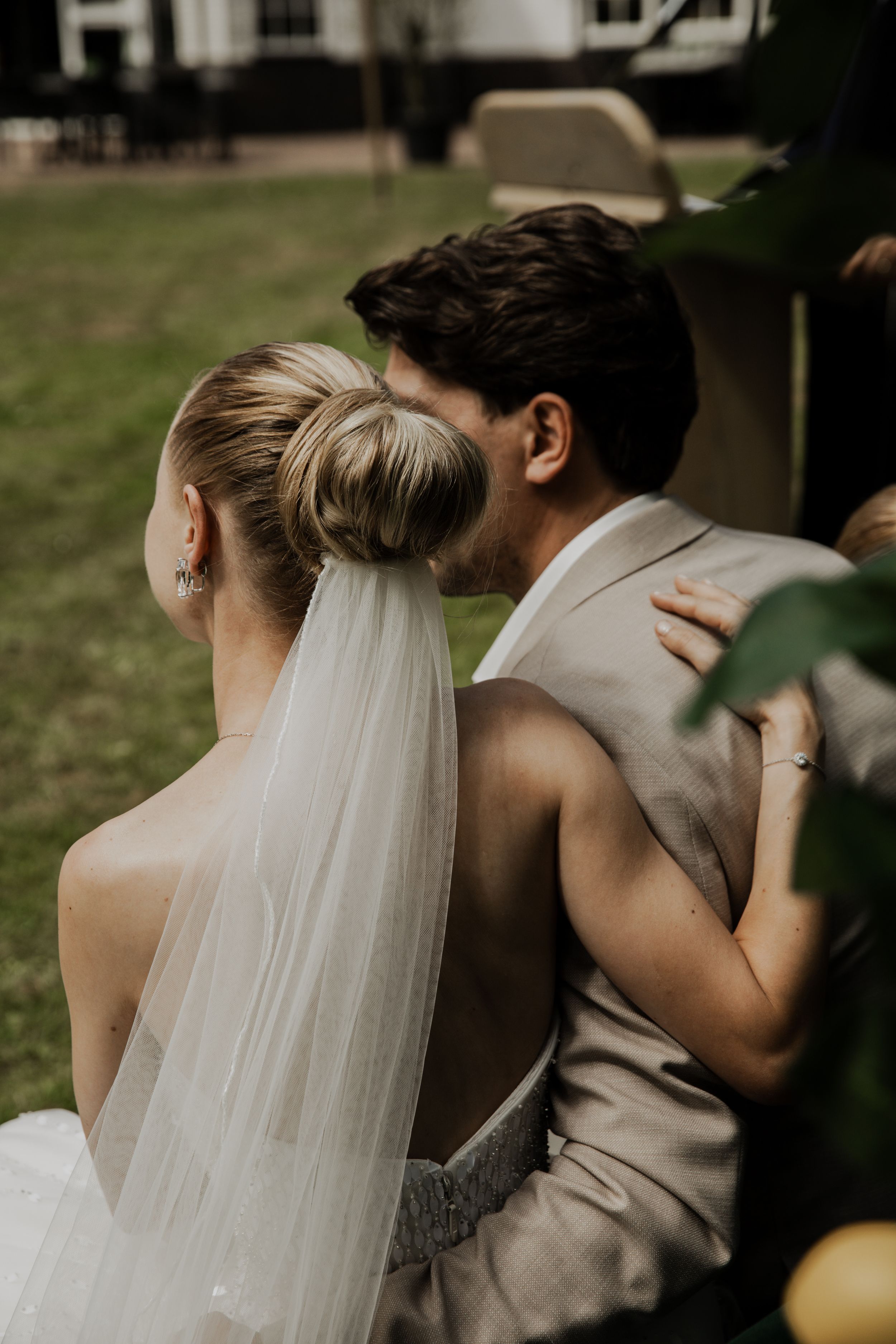 Bride and groom sitting closely together outdoors, bride wearing a veil and elegant updo.