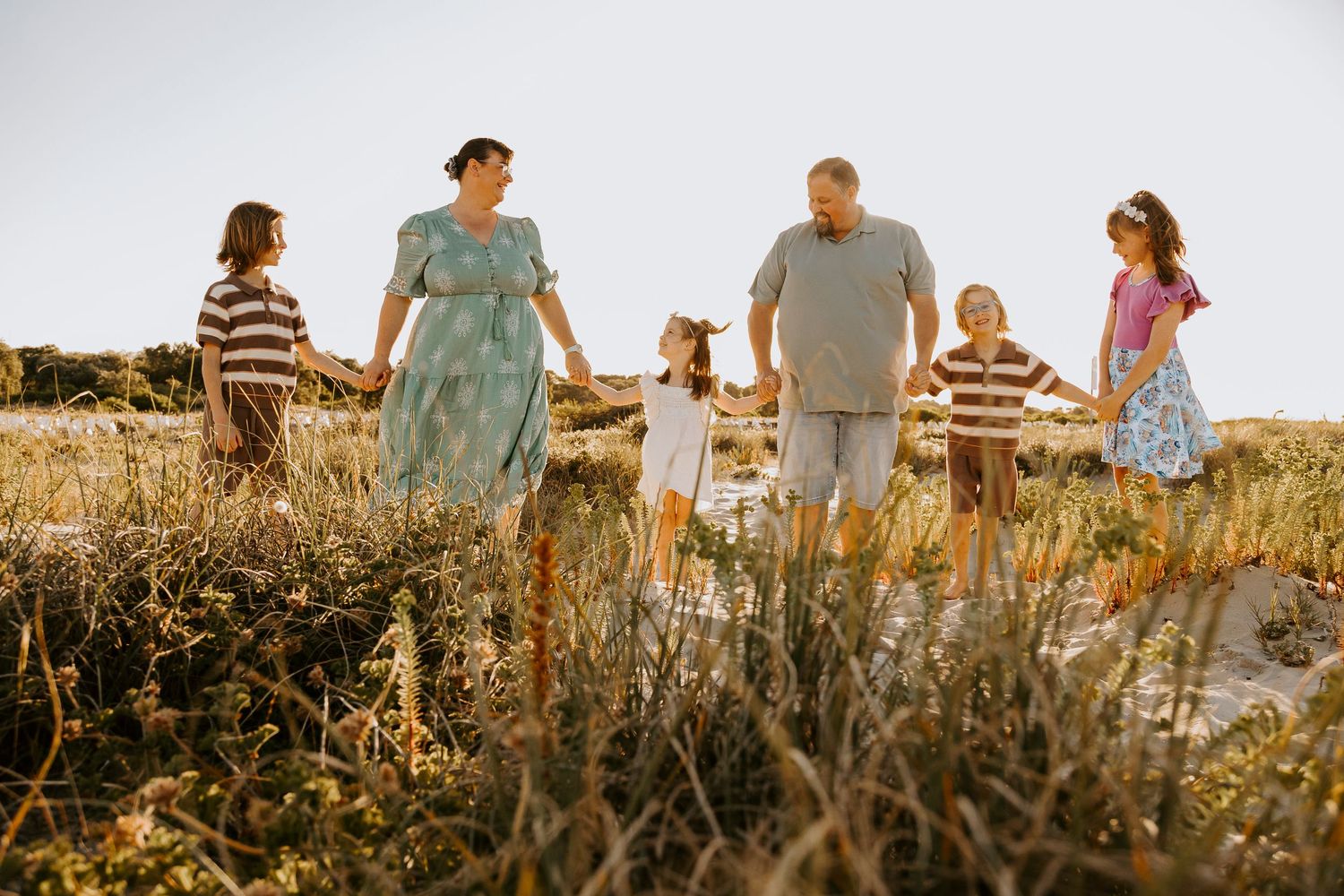 A group of people walk together through a golden field at sunset creating silhouettes against the warm sky.