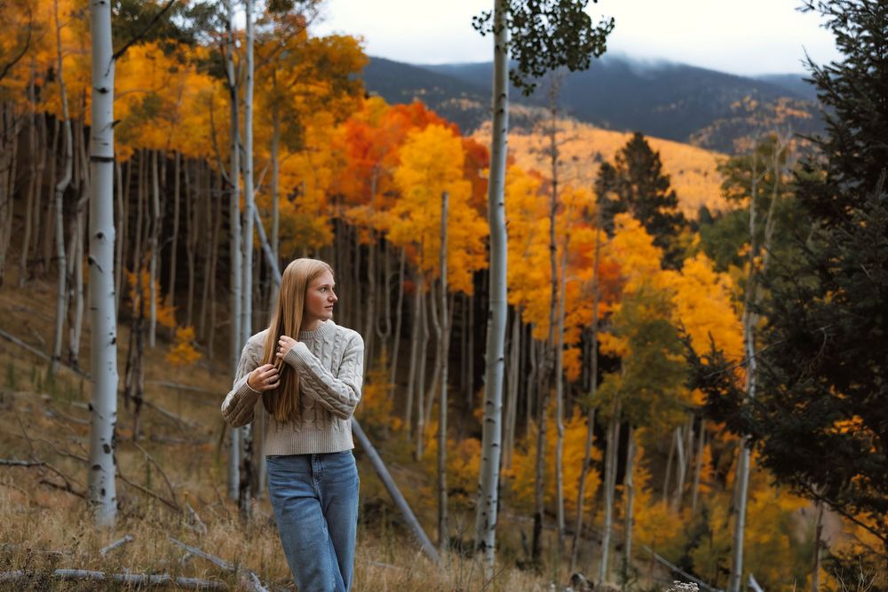 Santa Fe senior standing among vibrant autumn aspen trees on Santa Fe national forest hillside in fall.