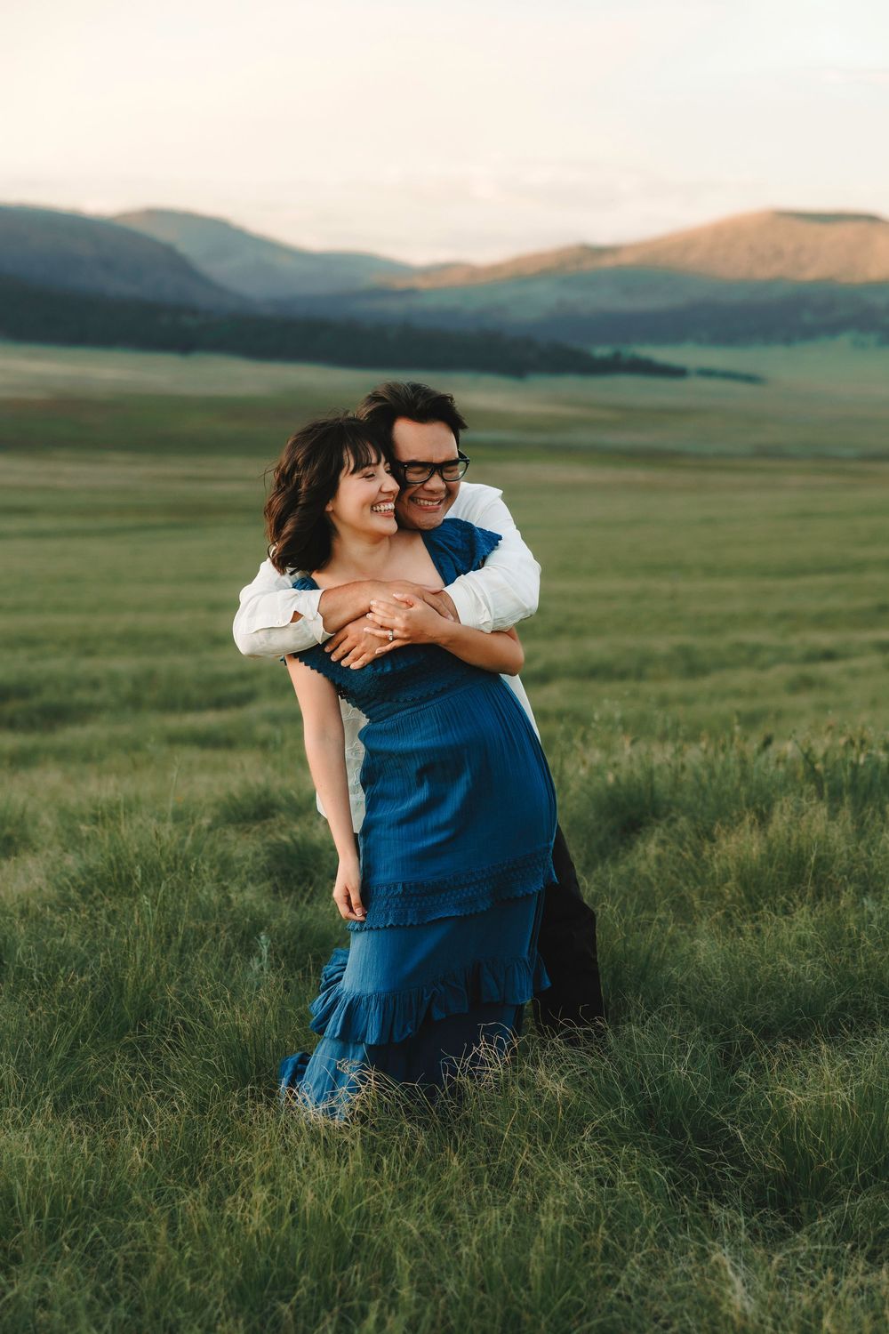 Santa Fe newly engaged couple embracing joyfully in lush green mountain meadow at sunset in the Valles Caldera.