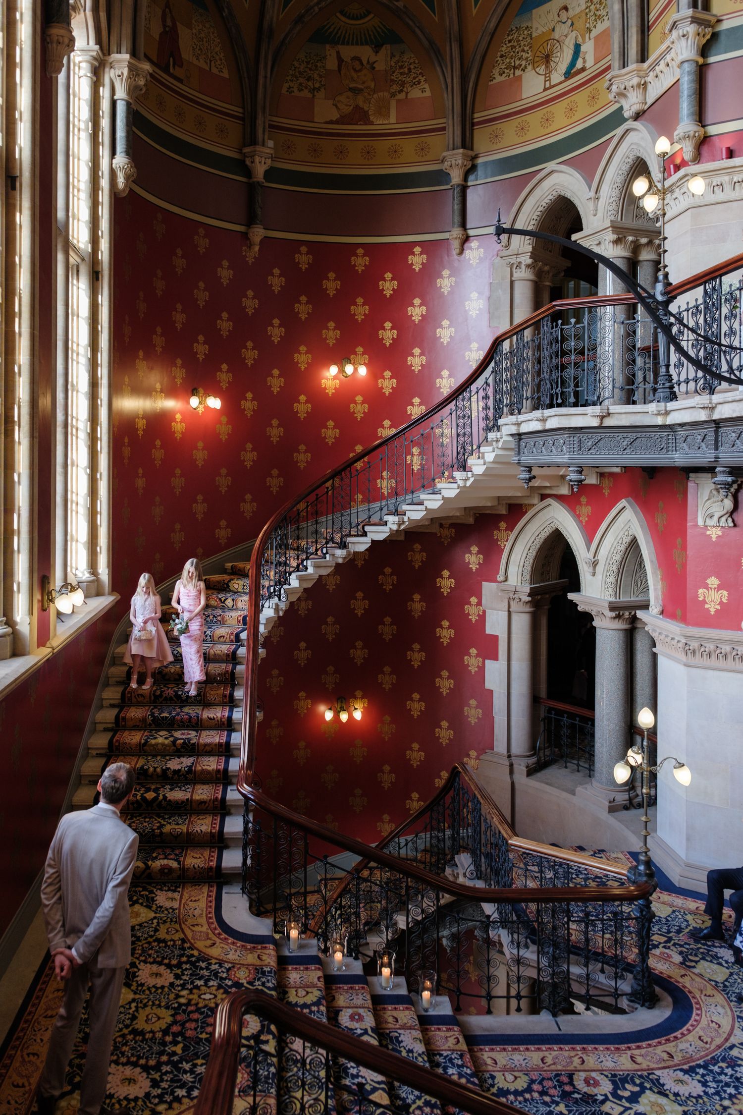 Elegant curved staircase with ornate red and gold Victorian interior design features wrought iron railings and wall sconces.