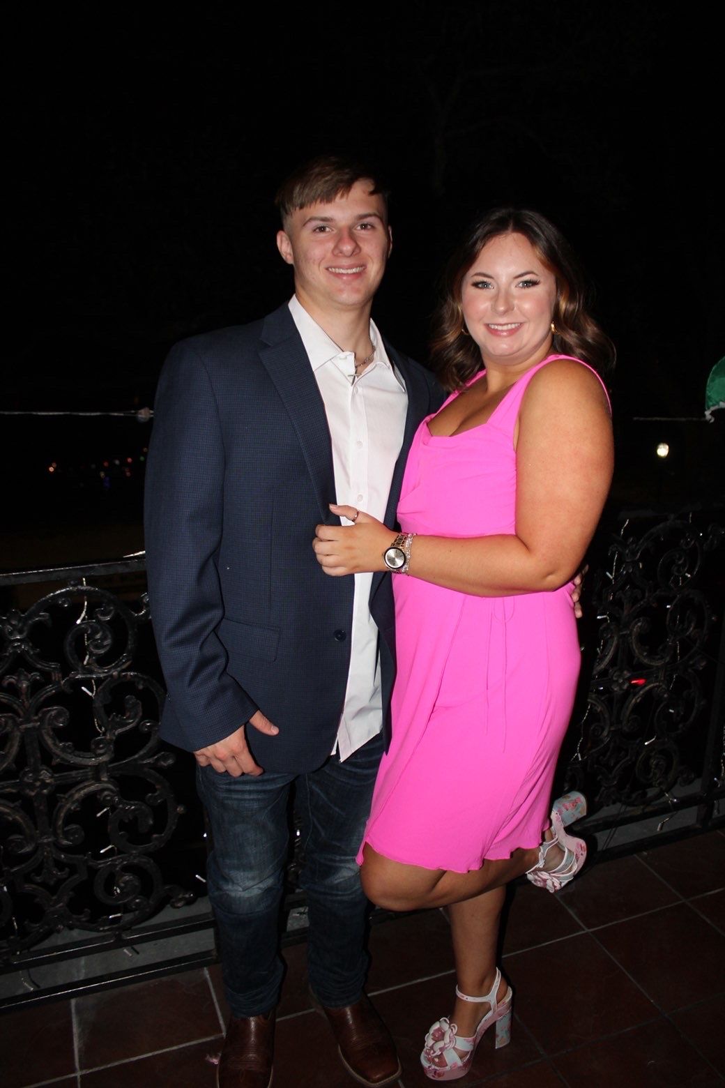 Couple in formal attire posing at night against dark background.