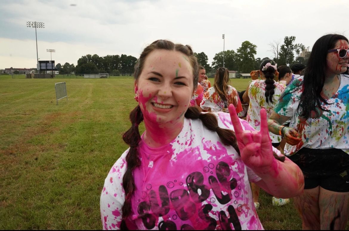 Group celebrating outdoors with pink color powder during daytime event.