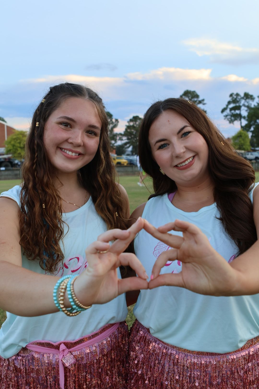 Friends making heart shapes with hands against blue sky background.
