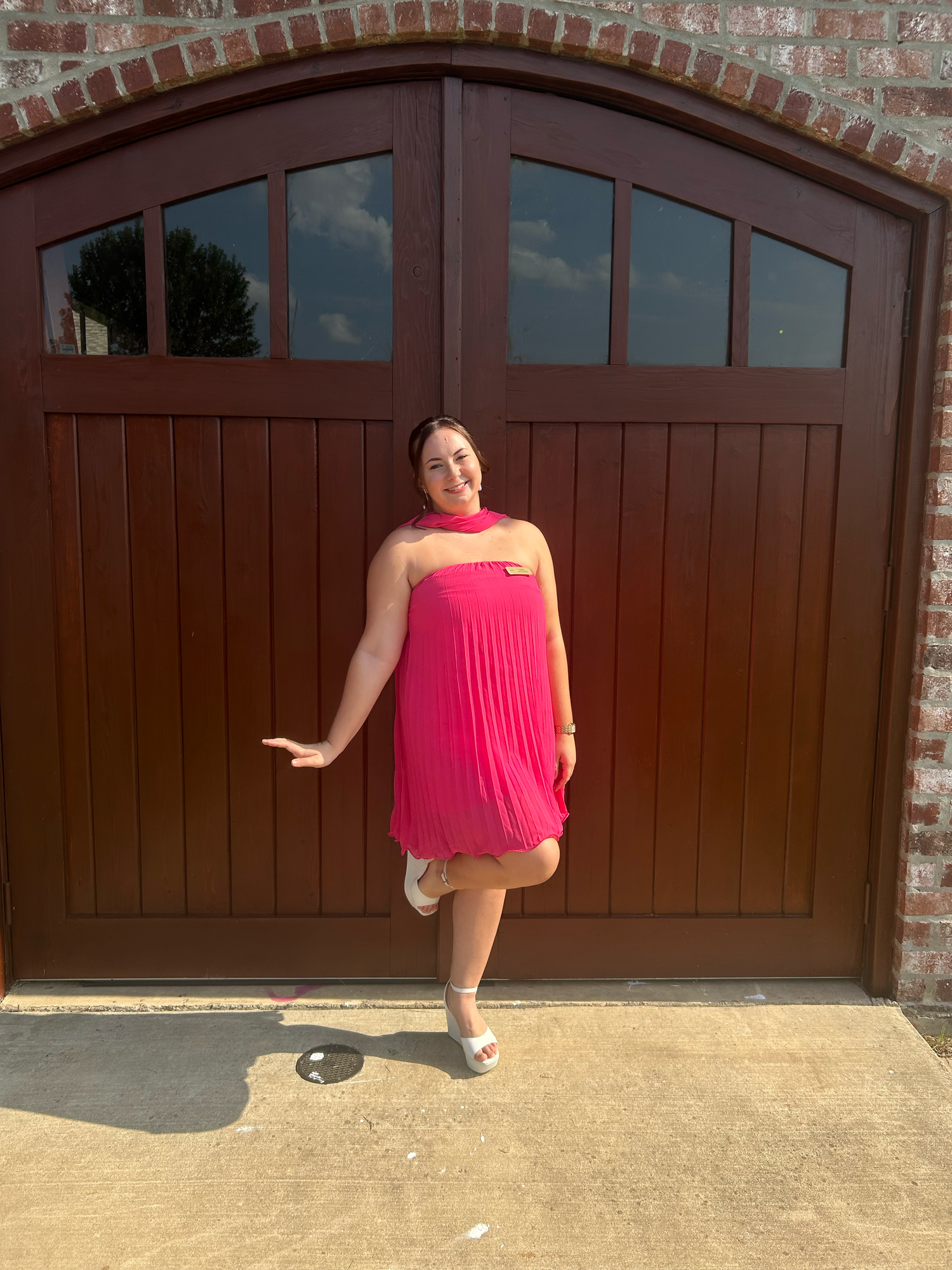 Person in bright pink dress posing playfully in front of wooden garage doors.