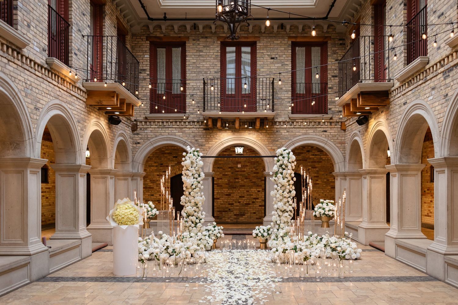 Elegant indoor wedding ceremony setup with white floral arrangements and arches in a luxurious marble hallway.