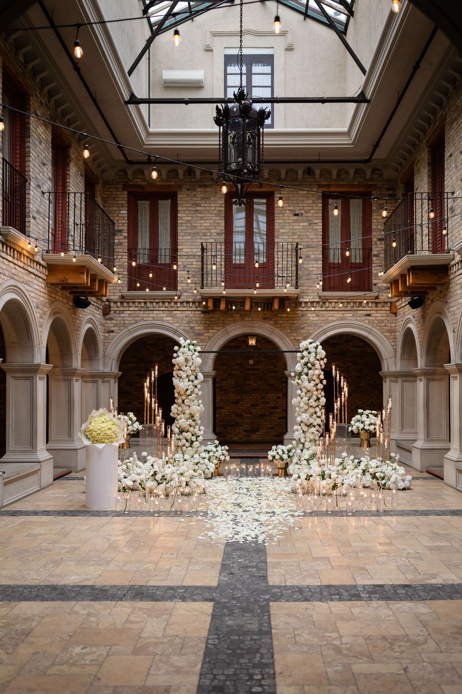 Elegant wedding ceremony setup in historic brick venue with white floral arrangements and hanging lights creating romantic ambiance.