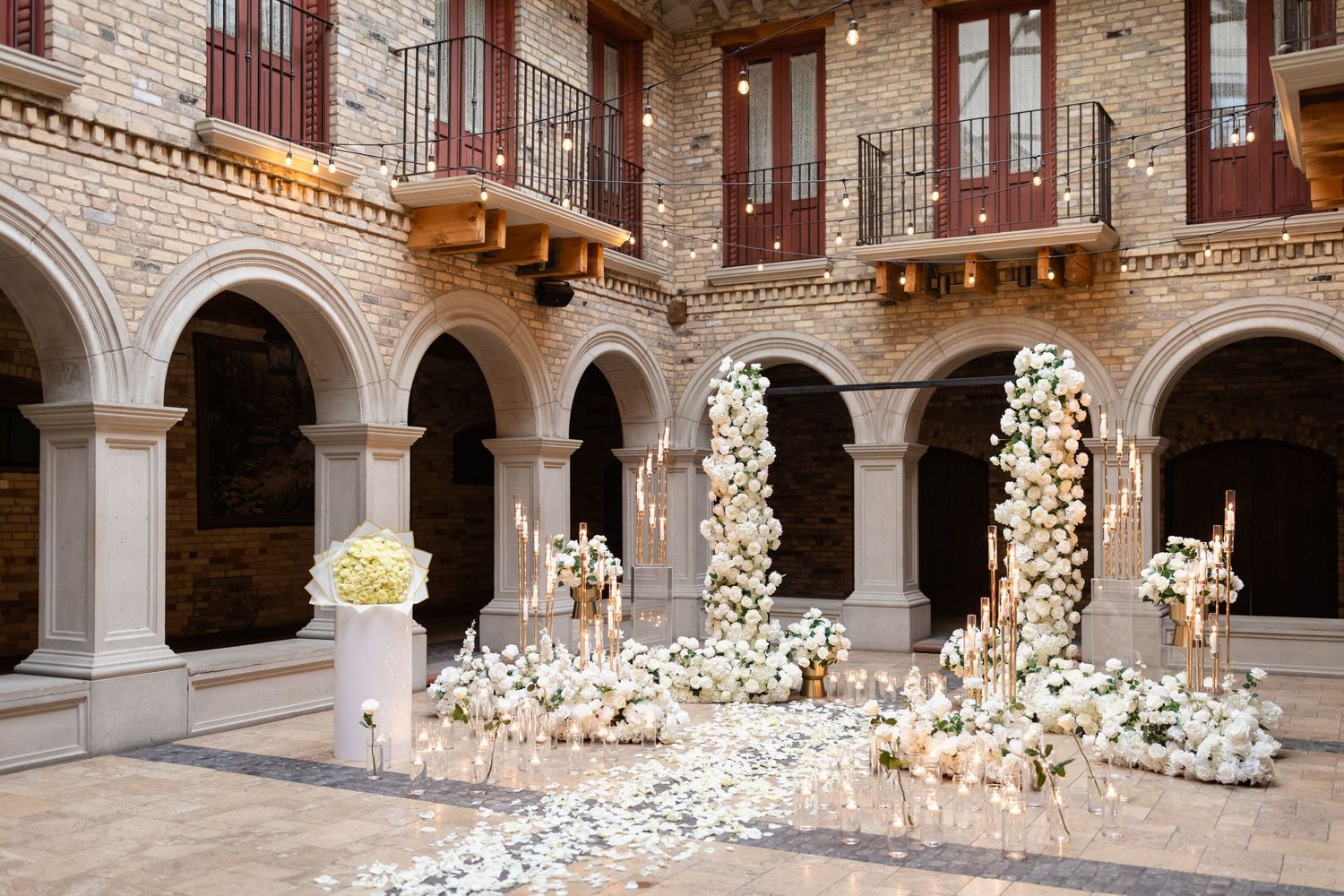 A stone courtyard features an elegant installation of illuminated white paper birds cascading from archways.