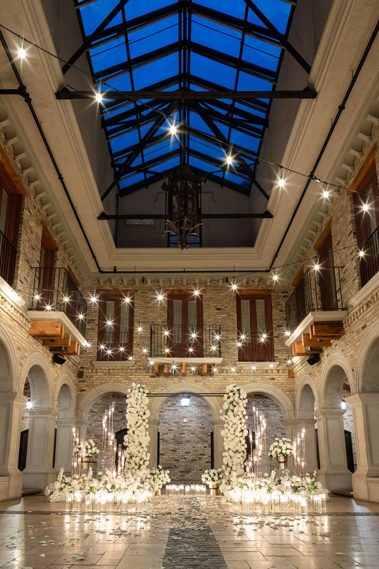Elegant wedding venue with glass ceiling, white pillars, and glowing string lights creating a magical indoor atmosphere.