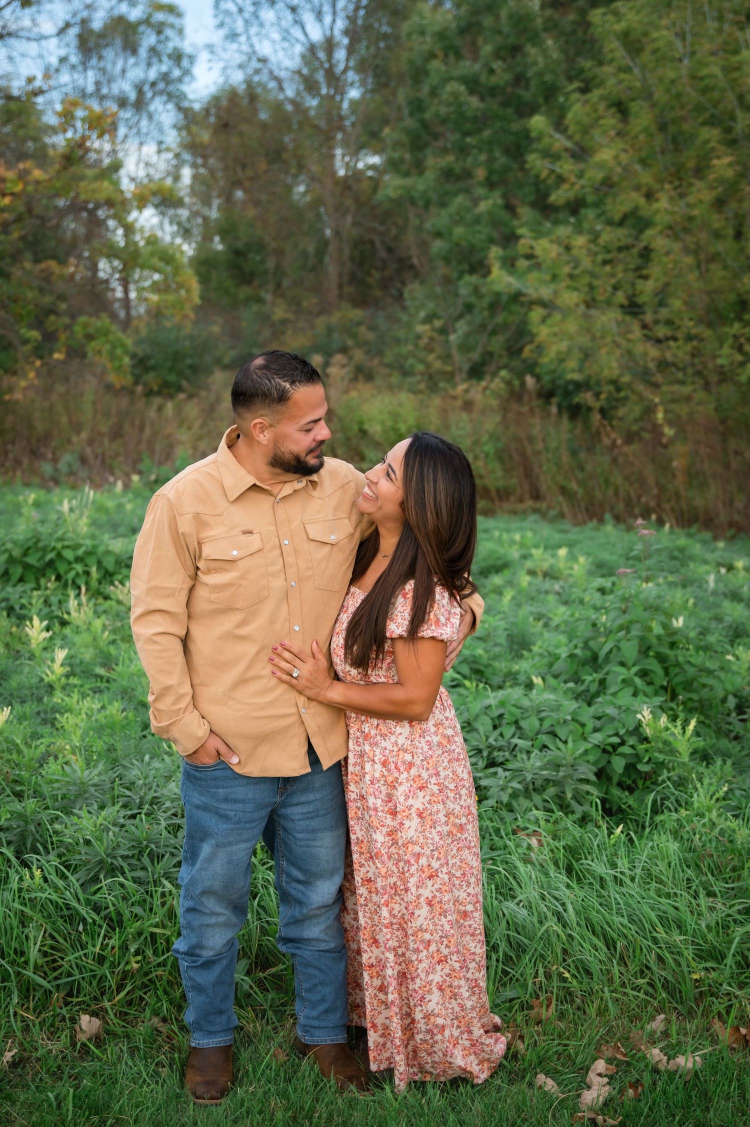 A couple shares an intimate moment together outdoors in a natural setting with green foliage and trees in the background.