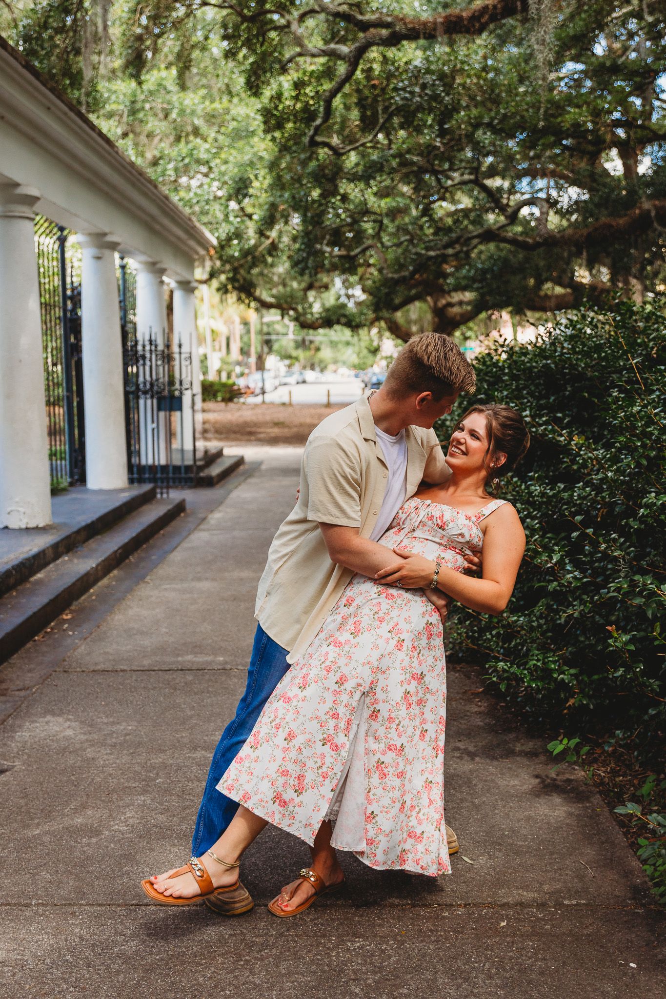 Romantic couple embracing on historic colonnade walkway with lush greenery.