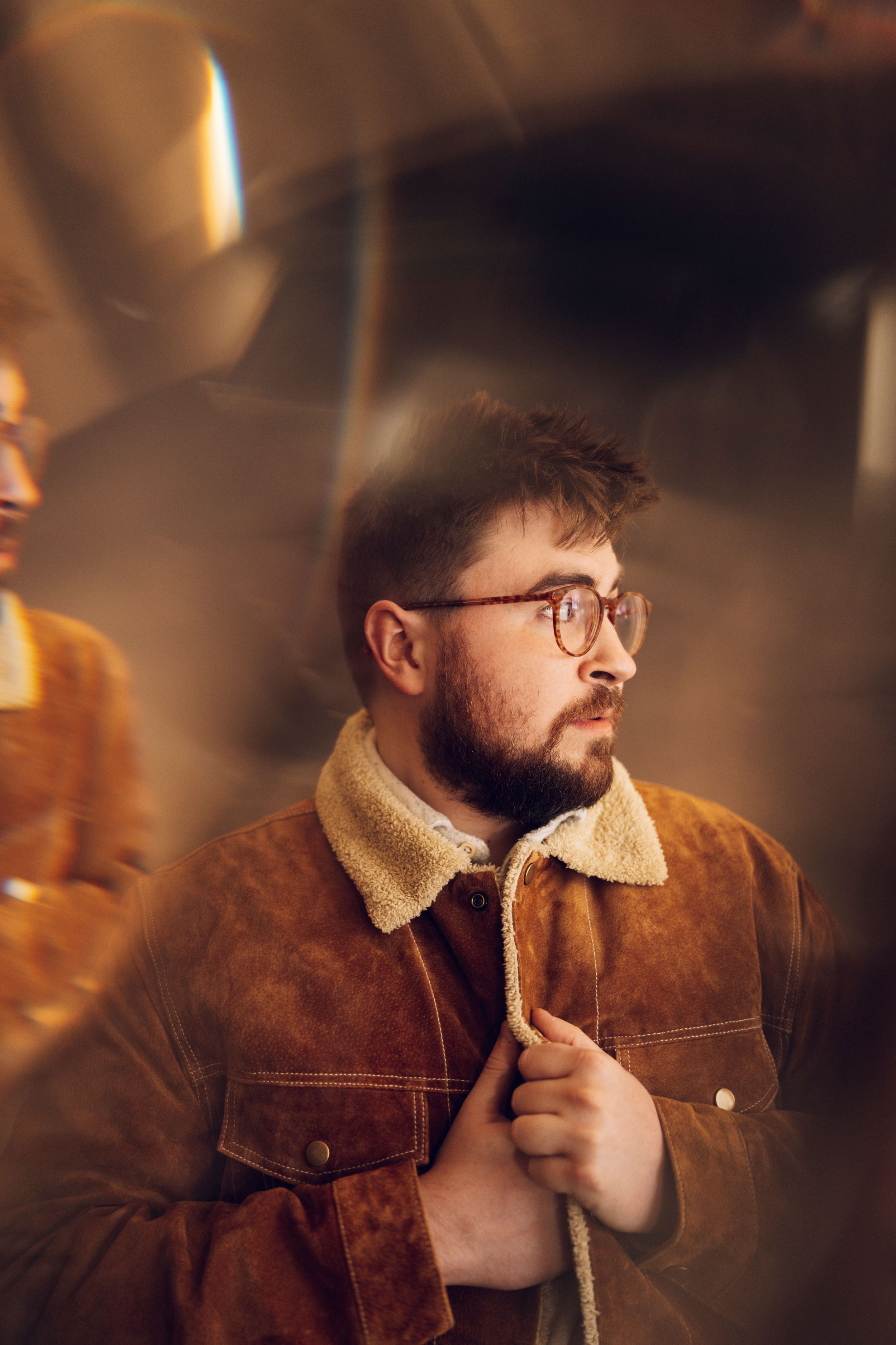 Portrait of a person in a brown corduroy jacket and glasses in warm ambient lighting.