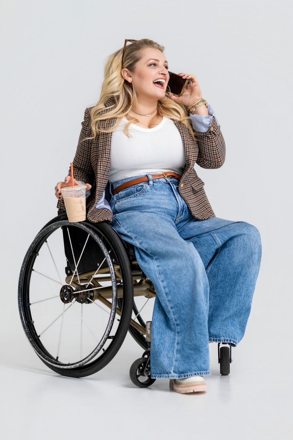 Person in wheelchair wearing cardigan and jeans while talking on phone against white background.