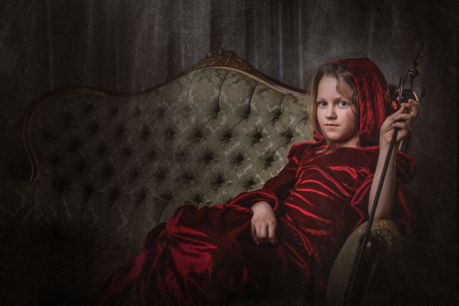 Dramatic portrait on vintage sofa featuring red velvet dress and moody lighting.