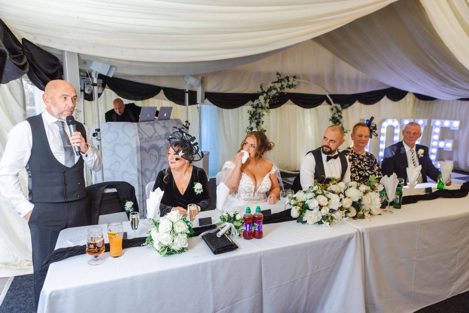 Wedding reception head table with elegant white floral decorations and draping.