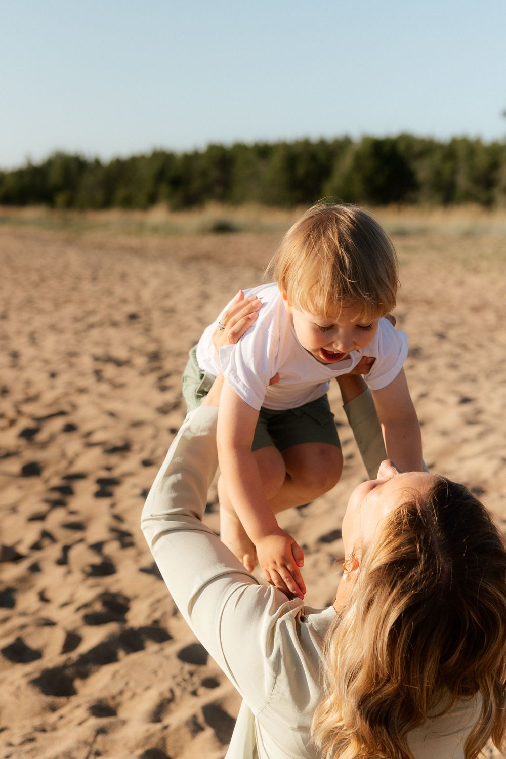 A tender moment between parent and child playing together on a sandy beach during golden hour.
