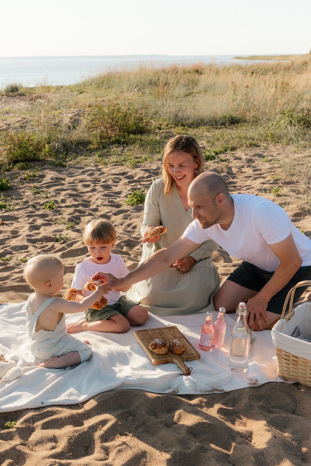 A family enjoys a beach picnic together on a blanket during golden hour at the seashore.