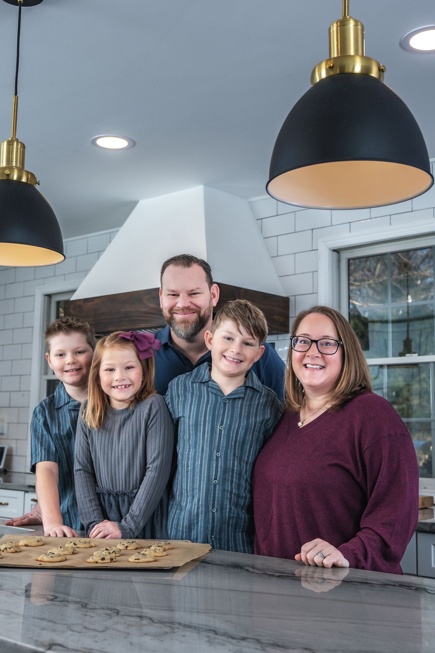 A family stands together in a modern kitchen with black pendant lights and subway tile backsplash.
