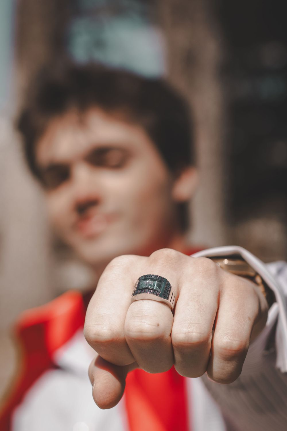 Close-up shot of a black class ring being displayed on someone's hand against a blurred background.