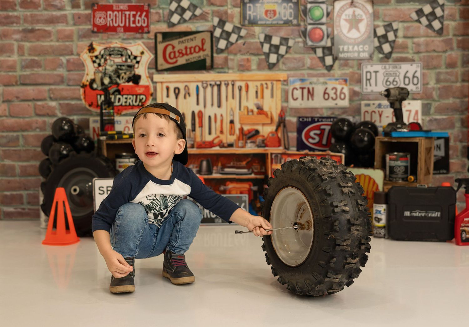 A vintage automotive-themed studio setting with retro signs, tools on pegboard, and a large tire prop on display.