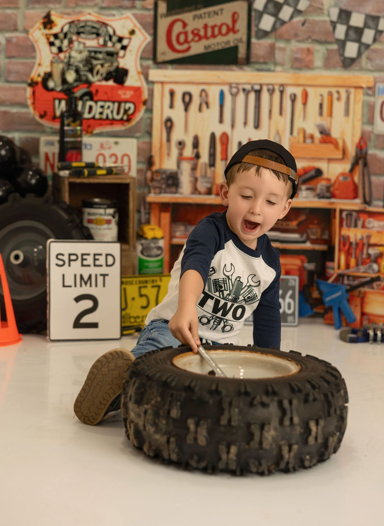 A young enthusiastic child explores an ATV tire in a vintage-styled garage workshop decorated with automotive memorabilia.