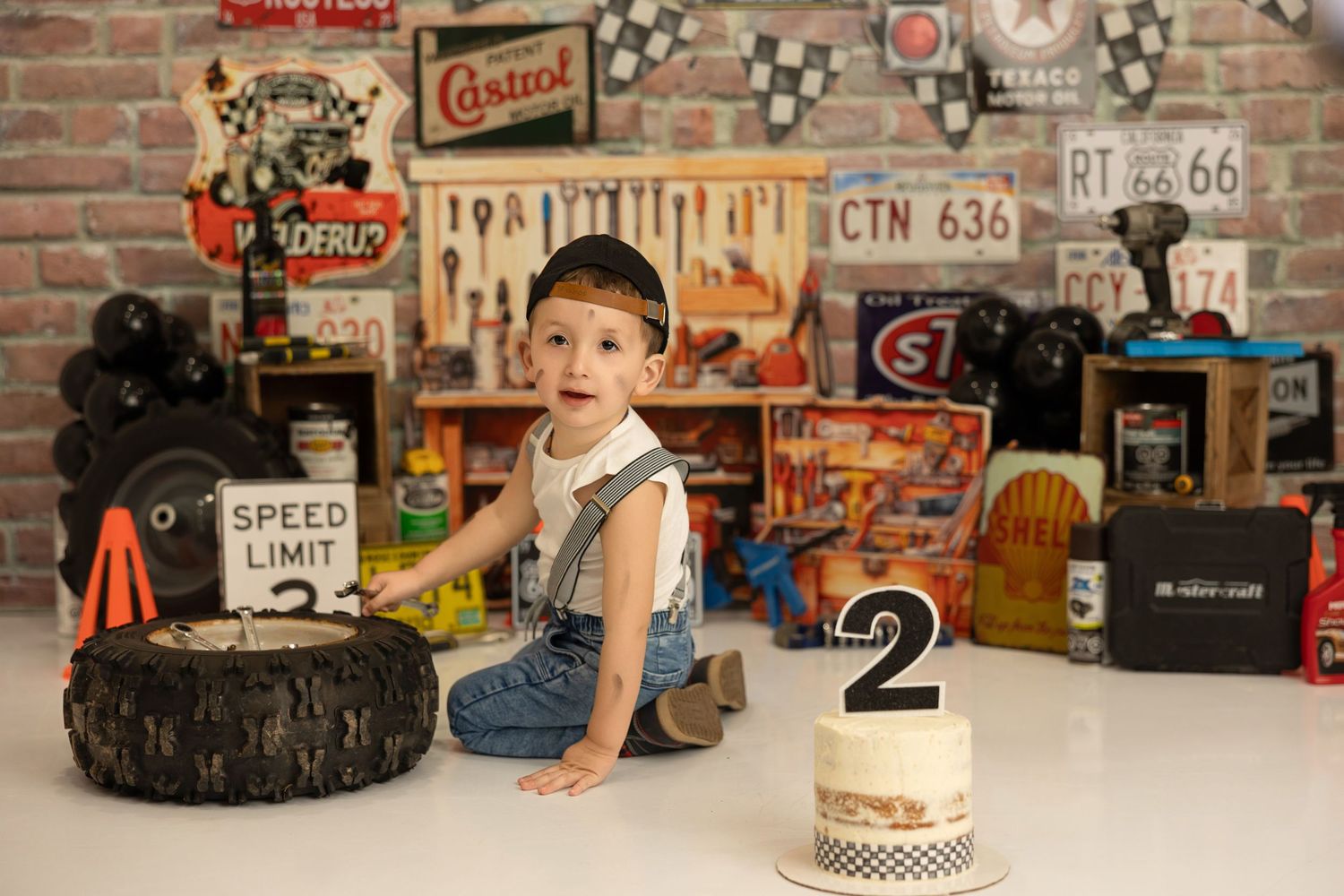A birthday setup with a number 2 cake and tire prop against vintage automotive decor and brick wall.