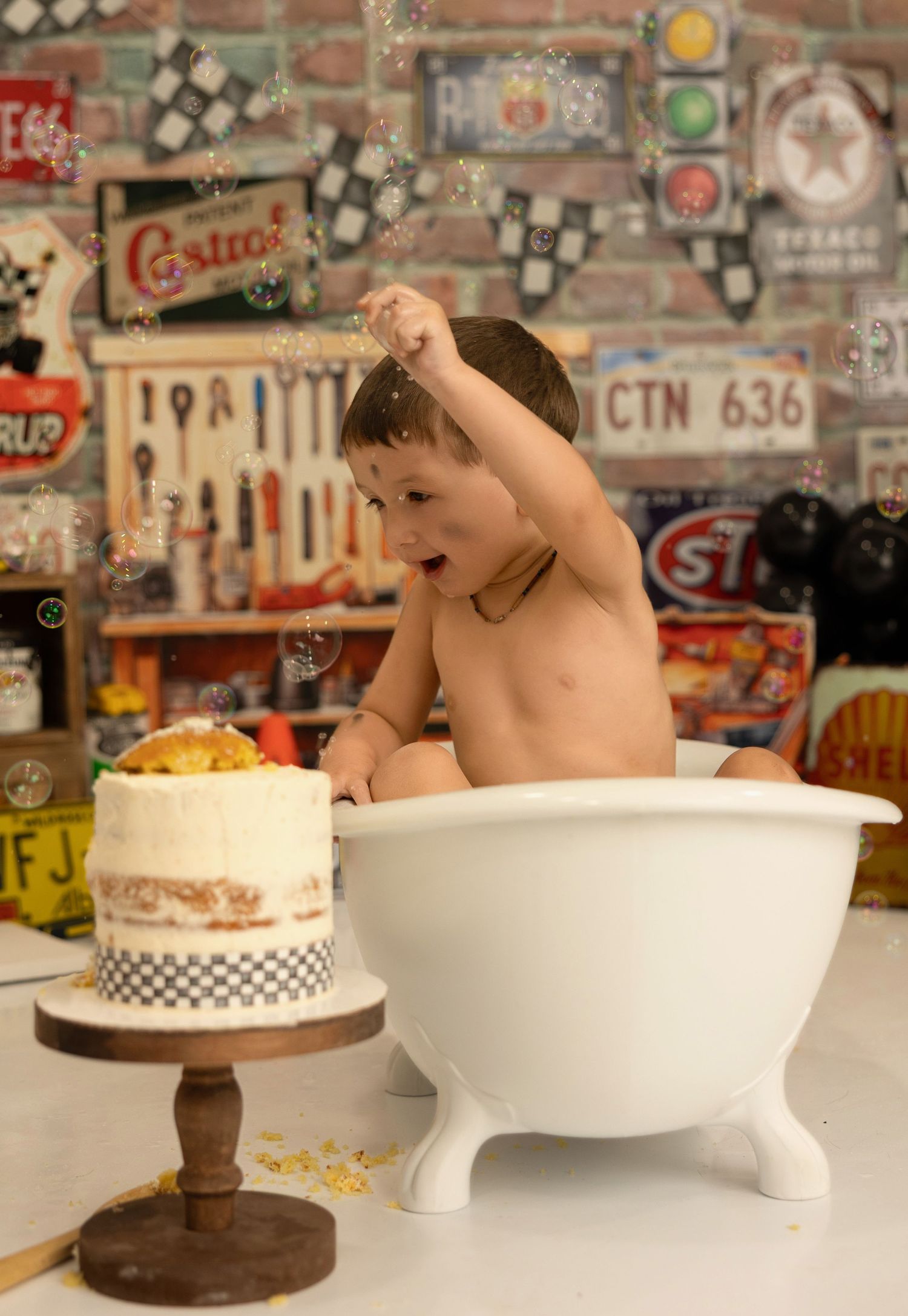 A bath time scene with cake and automotive-themed backdrop featuring vintage signs and tools on brick wall.