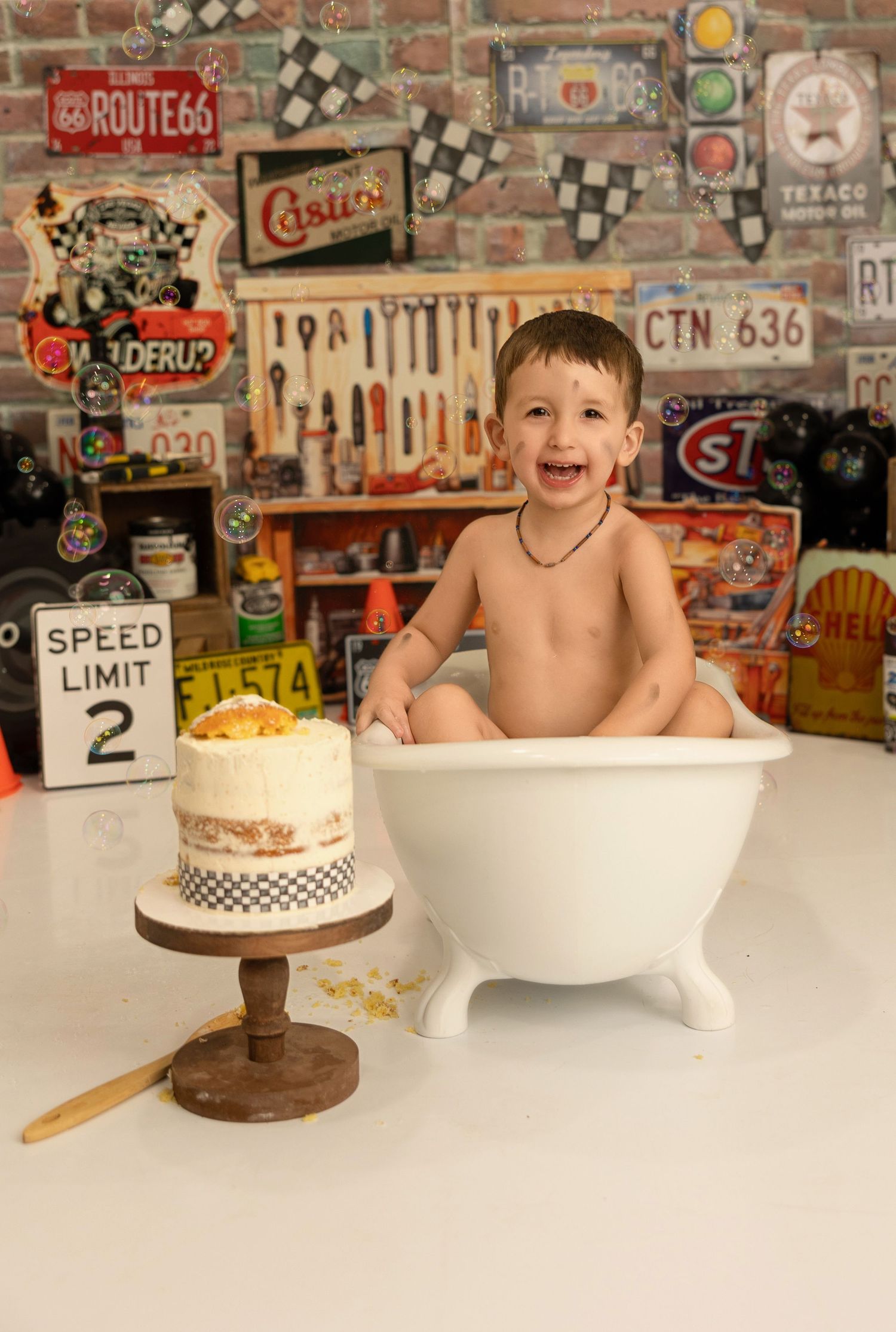 A cake smash photo setup with white bathtub and birthday cake against vintage garage themed backdrop.