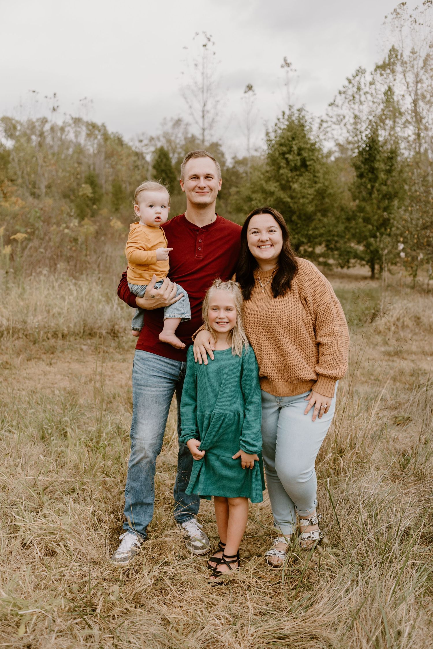 A family wearing casual attire poses together in a grassy outdoor field during golden hour.