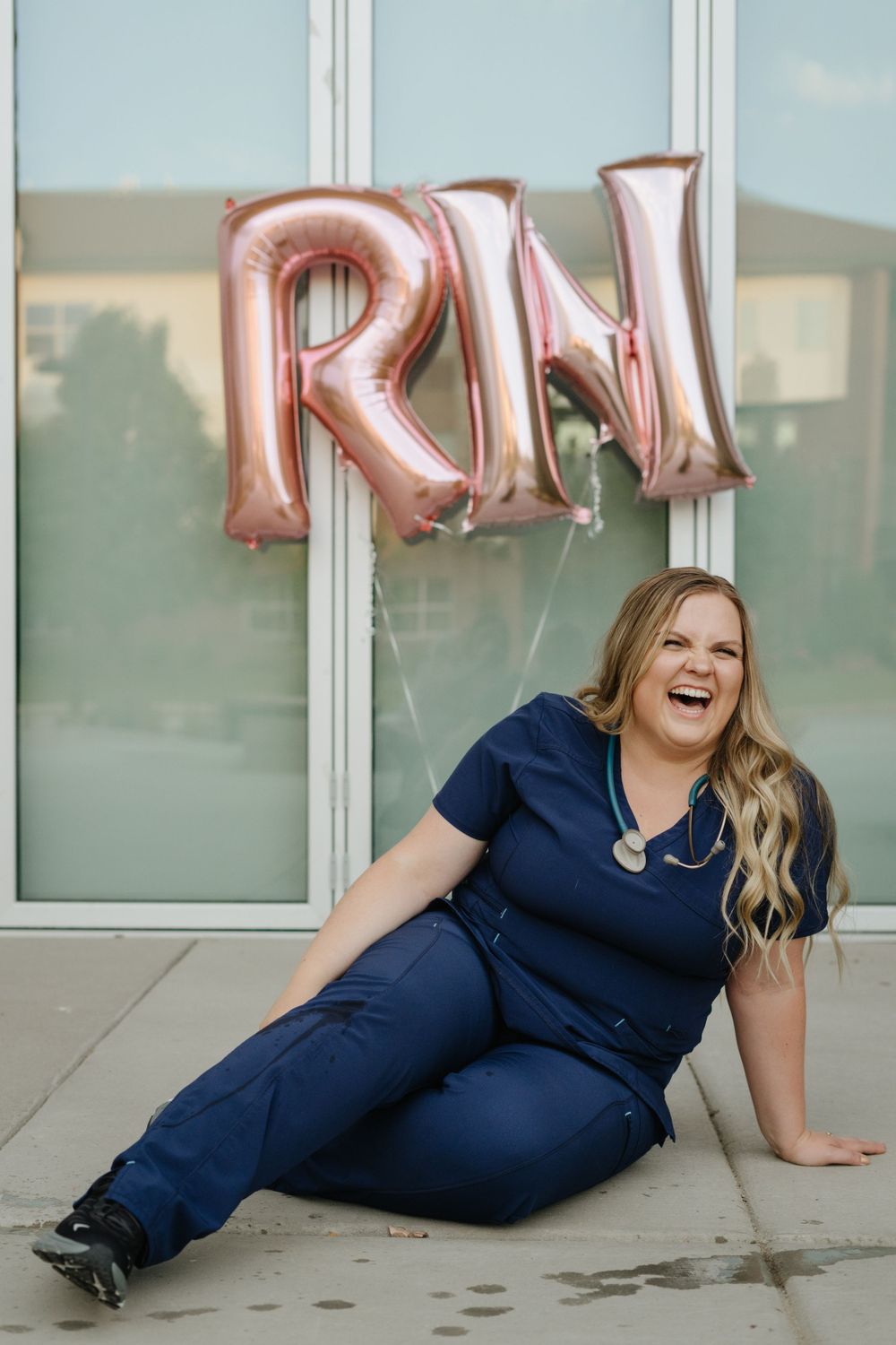 Nurse in blue scrubs poses with rose gold RN balloons in celebration.