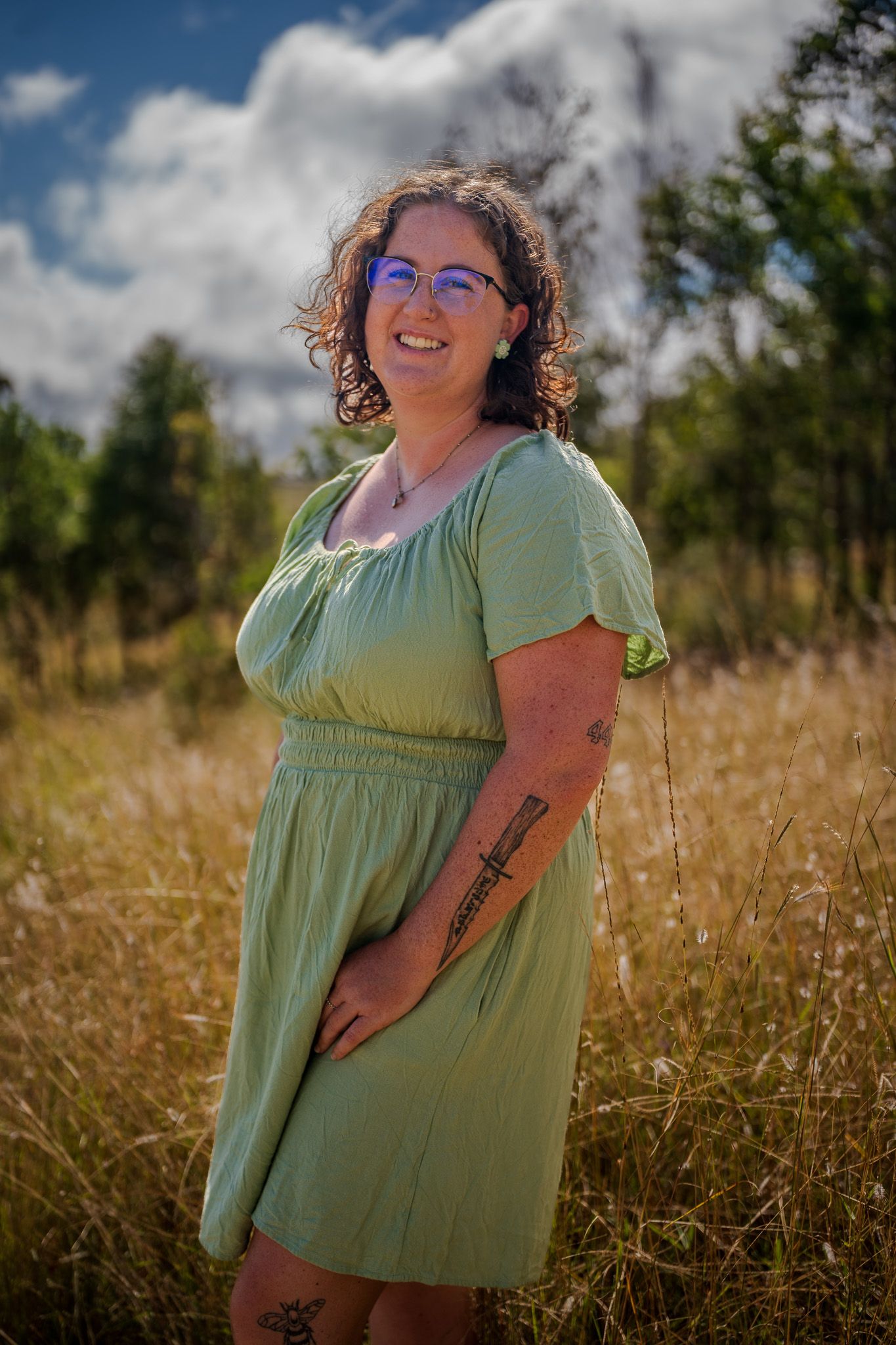 Person in green dress standing in sunlit meadow with fluffy clouds in background.