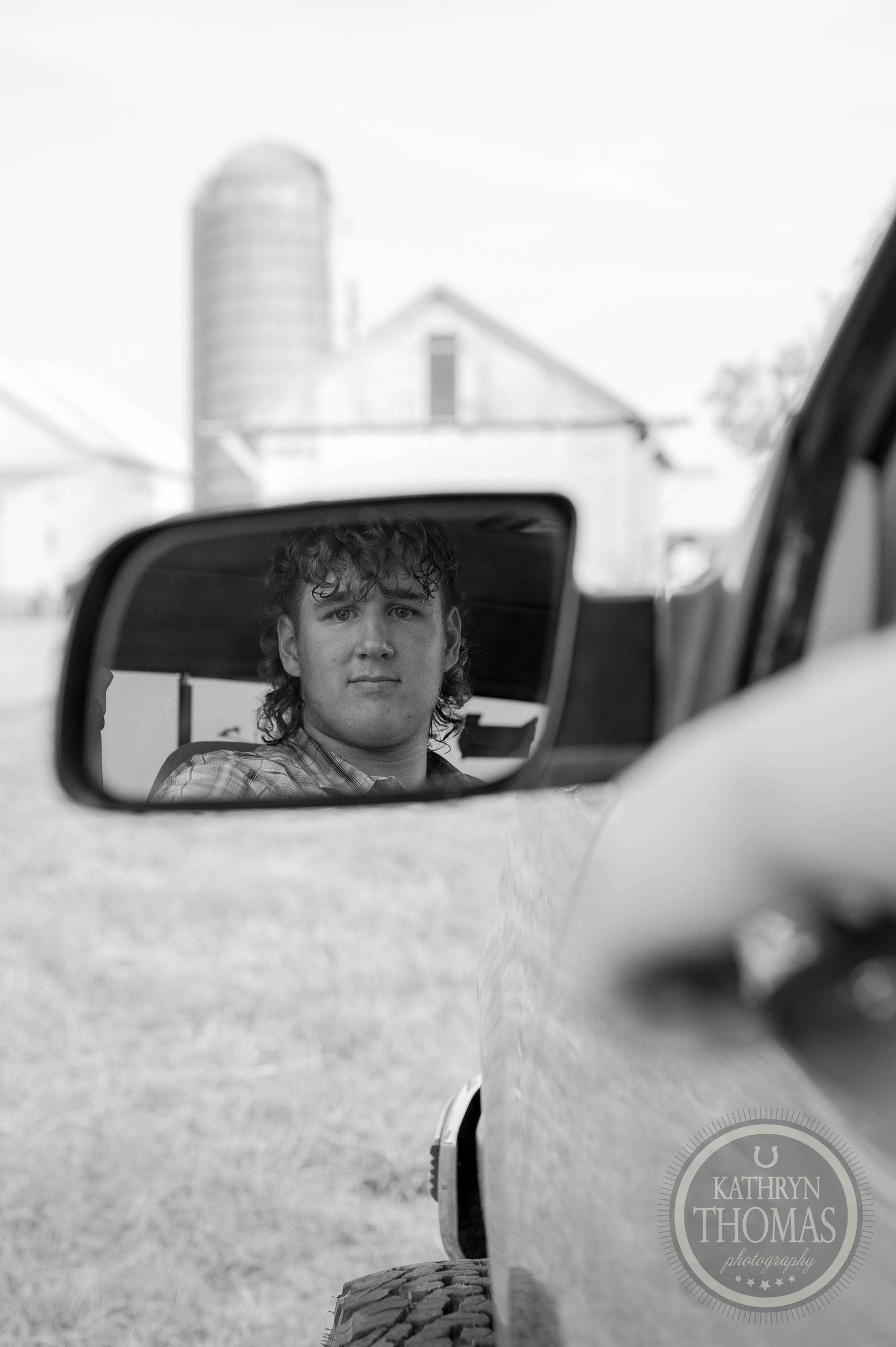 Black and white reflection in a side mirror showing a farm silo in the background.