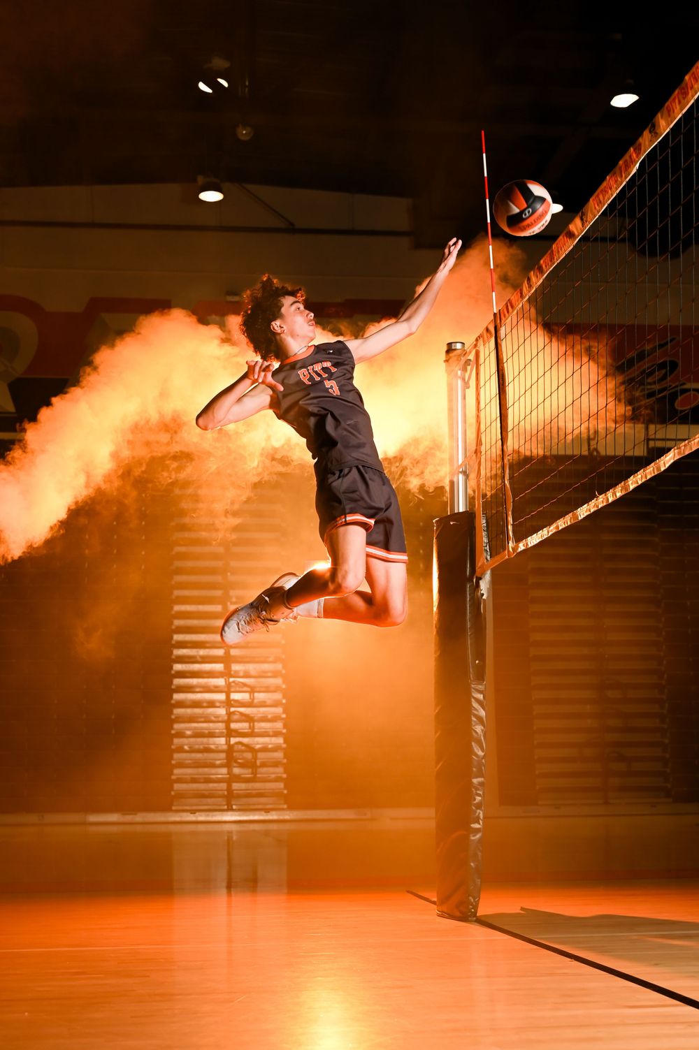 Volleyball player leaps for a spike against an orange-lit background.
