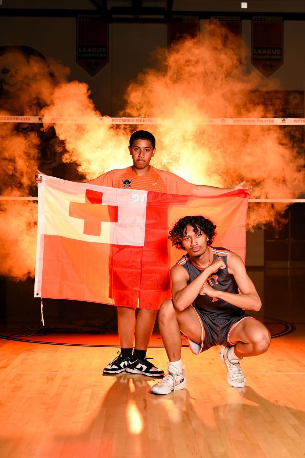 Athletes pose on a basketball court with orange smoke effects in the background.