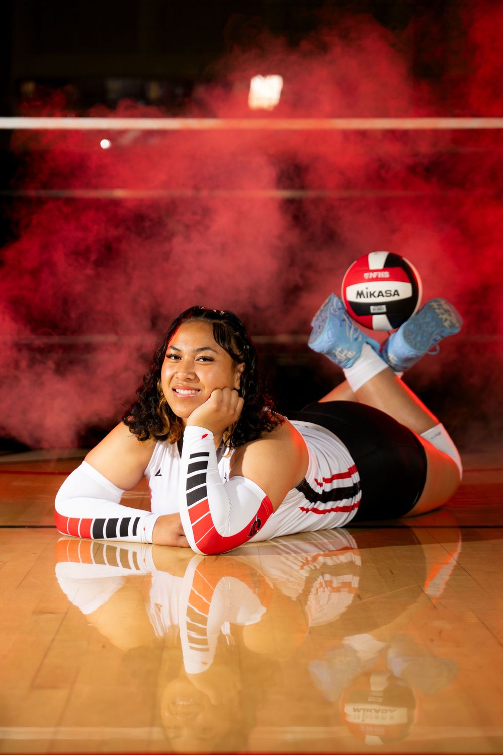 Player lies on wooden court floor in white uniform with red smoke effects in background.