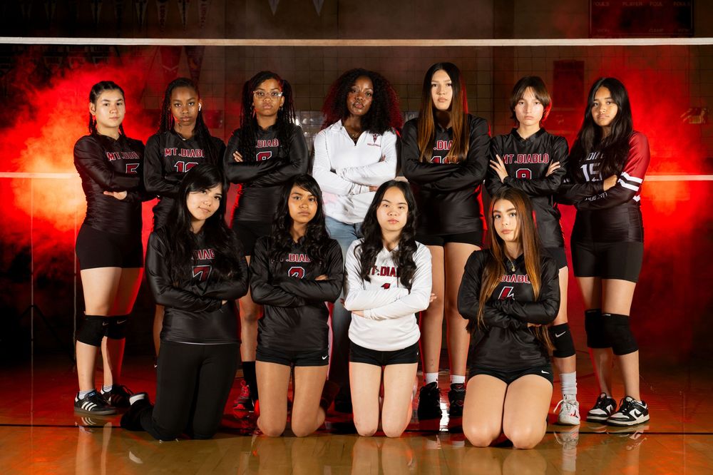 Volleyball team members pose together on court floor with red lighting effects.