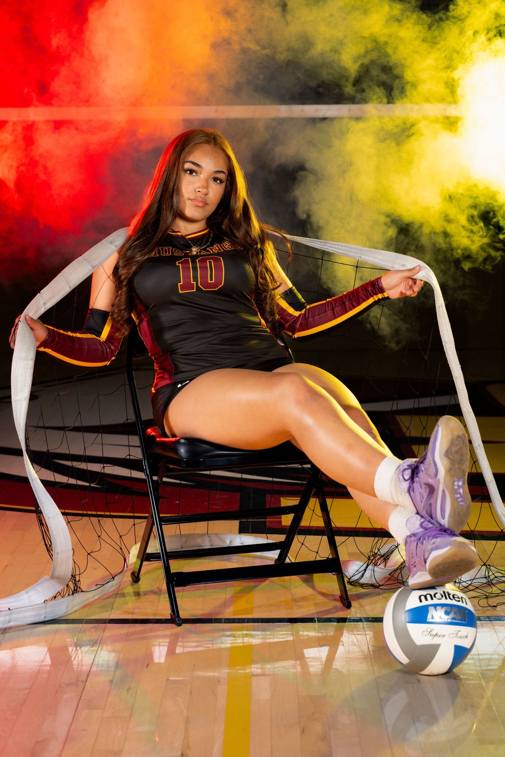 Volleyball player stretches on court floor with dramatic lighting and volleyball nearby.
