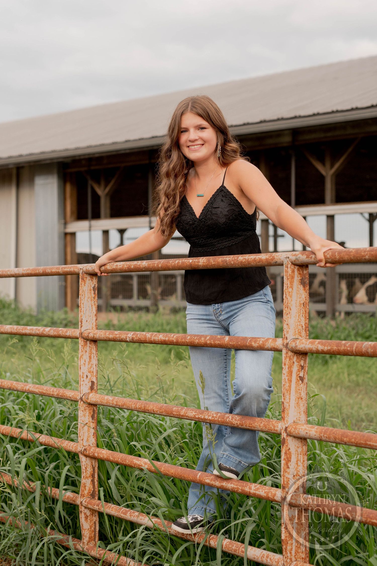Casual country portrait against wooden fence with barn in background.