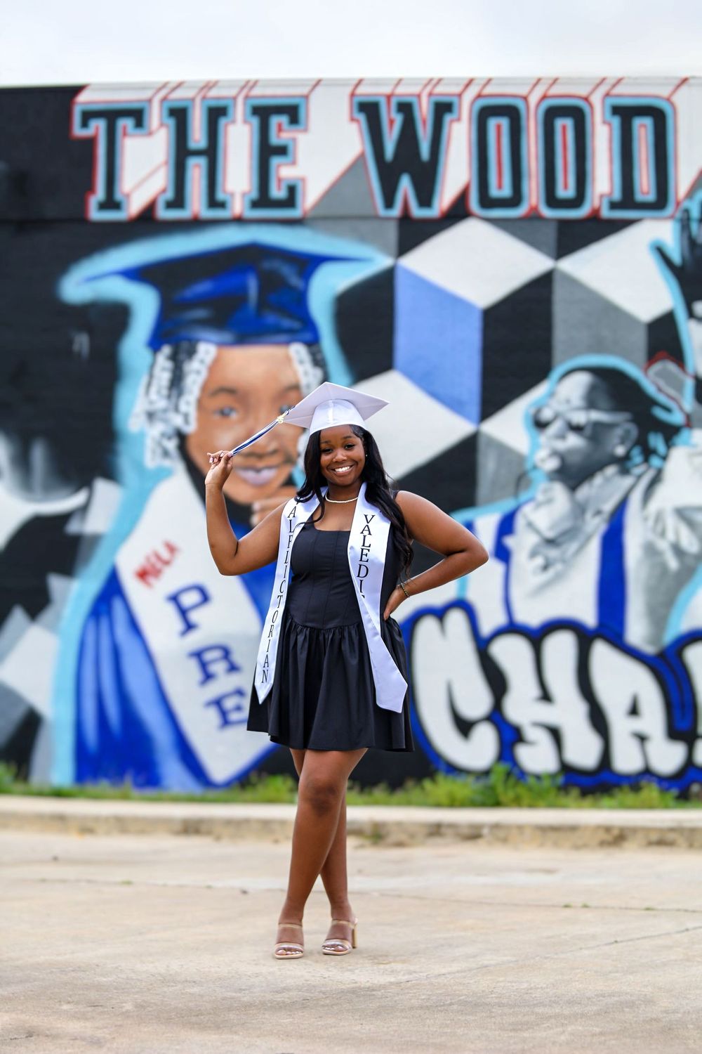 Young child in navy dress poses playfully against urban graffiti wall with blue and white artwork.