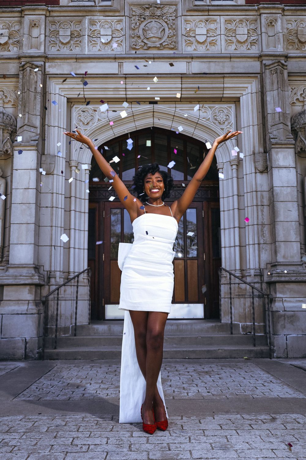 A celebratory scene in front of an ornate stone doorway features a joyful figure in a white dress and red heels with arms raised.