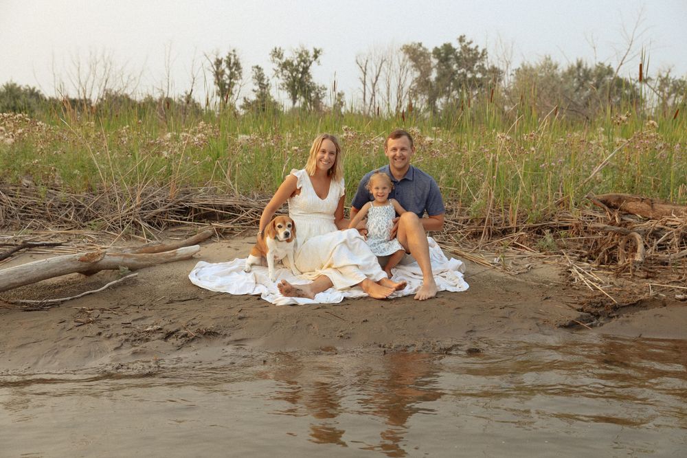 Family photoshoot on a beach with driftwood and natural coastal elements.