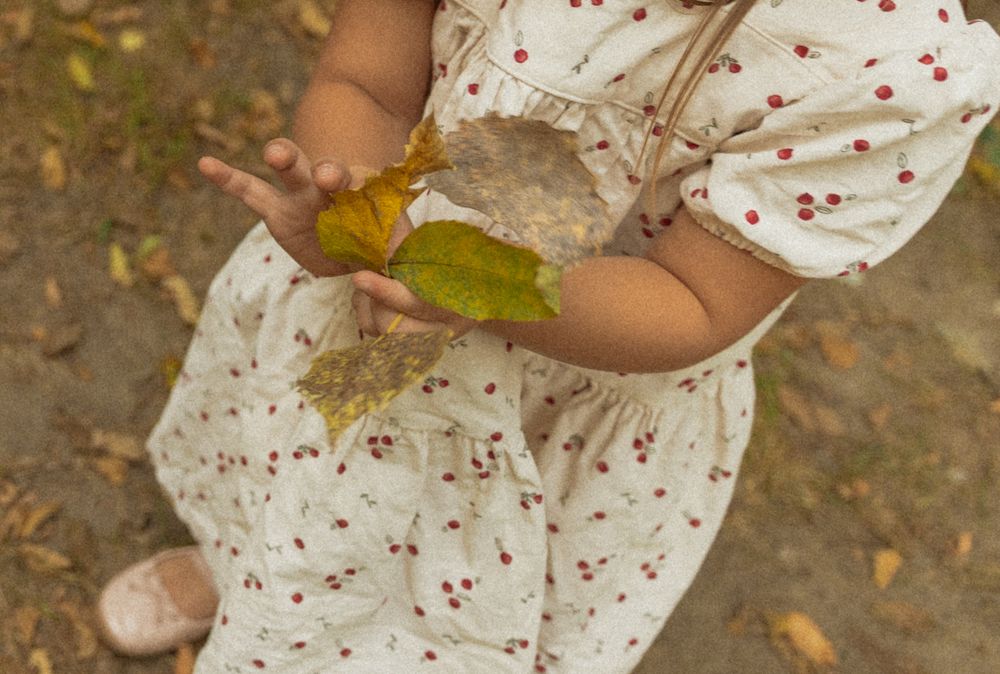 Close-up details of a white dress with red polka dots against autumn leaves.