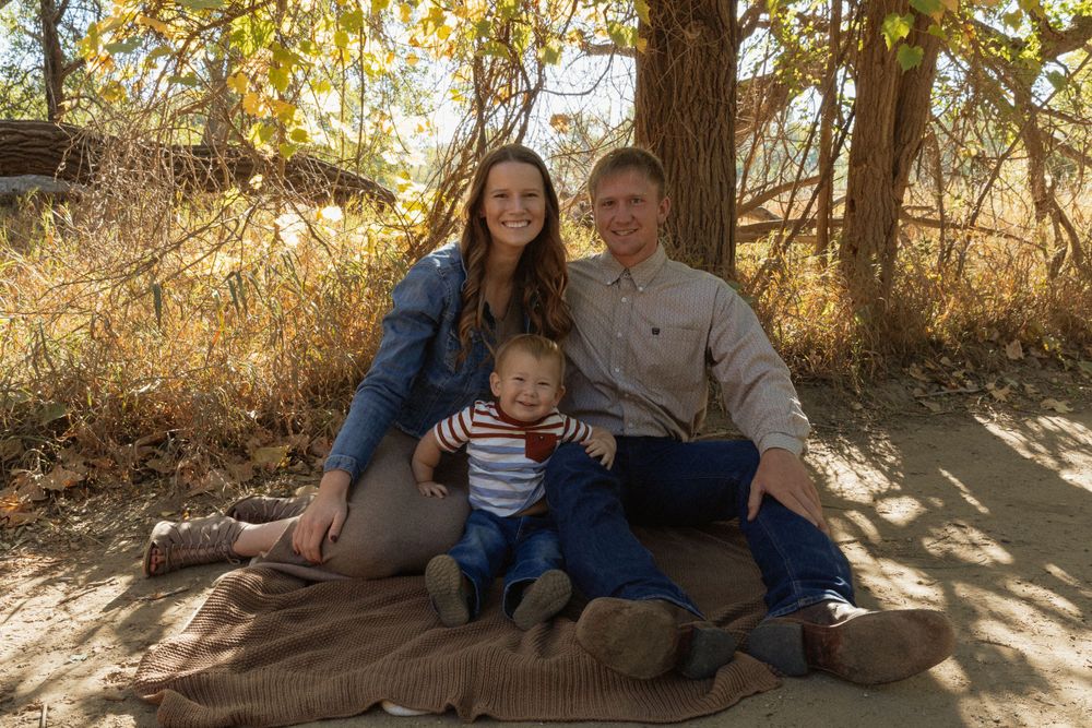 A family poses together on a wooded path during autumn with golden foliage in the background.