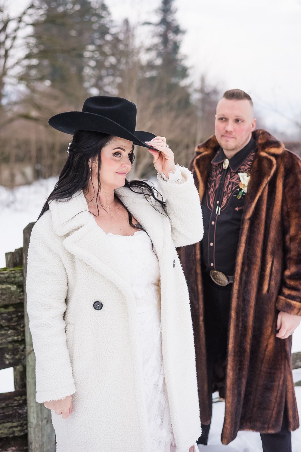 A bride tries on a cowboy hat while her new husband watches lovingly nearby.