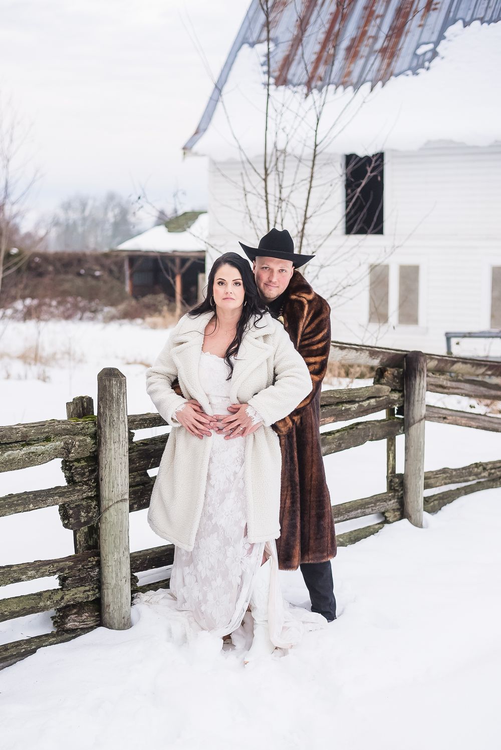 A groom with his arms around his new bride at their snowy, rustic, barn venue.