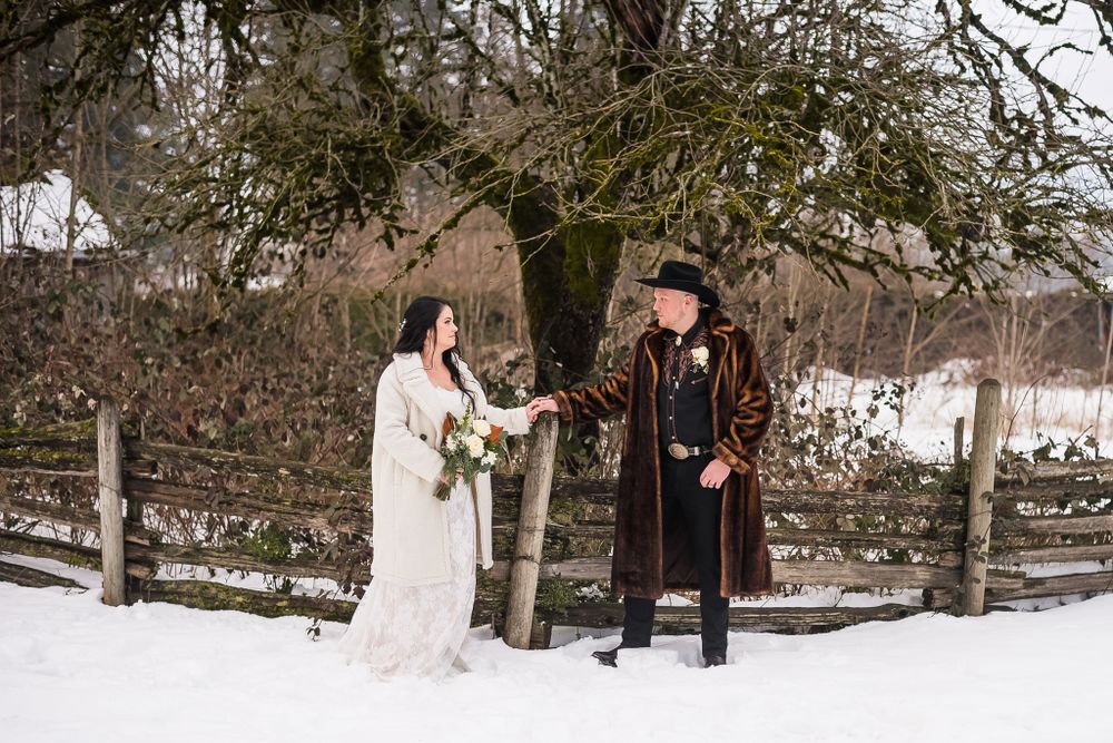 A bride and groom pose by a fence and the snow covered ground at their wedding venue in Langley, BC.
